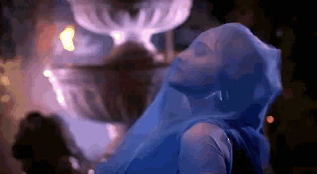 a woman is covered in a blue cloth and is dancing in front of a fountain .