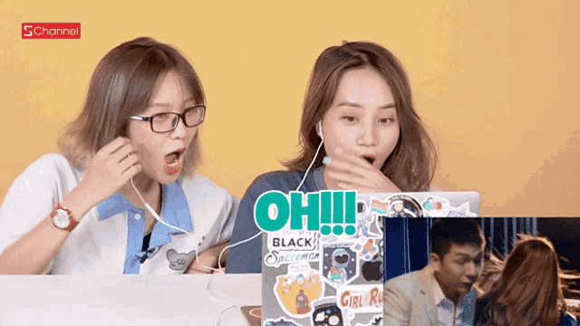 two women are sitting at a table with a laptop that says oh on it
