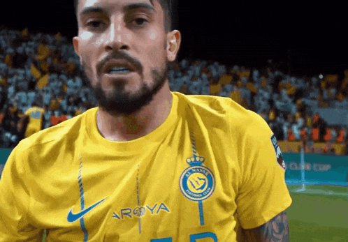 a man with a beard wears a yellow shirt that says arya on it