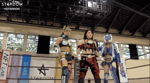 three female wrestlers are standing in front of a stardom banner