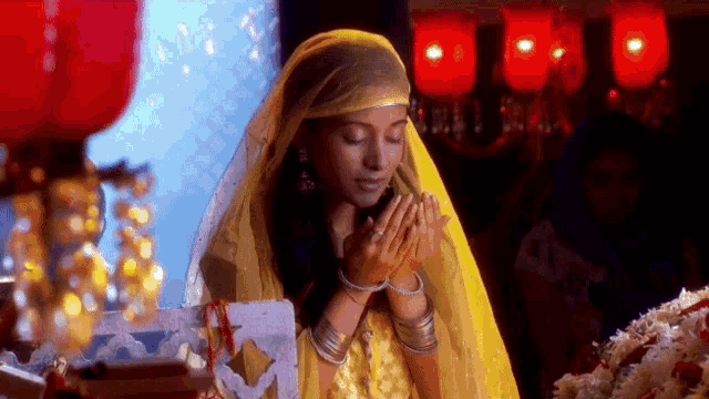 a woman in a yellow dress praying with her hands together
