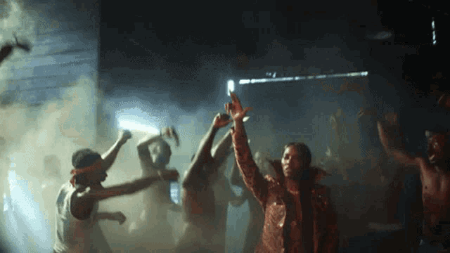 a group of people are dancing in a dark room with smoke coming out of it