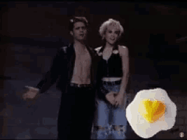 a man and a woman are dancing in front of a large fried egg