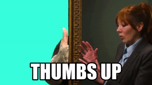 a woman in a suit holds her hands up in front of a picture frame with the words thumbs up below her