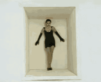 a woman in a black dress and black gloves is standing in a box with her arms outstretched .