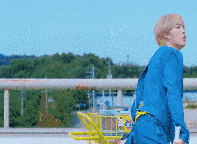 a man in a blue denim jacket is walking with a yellow cart