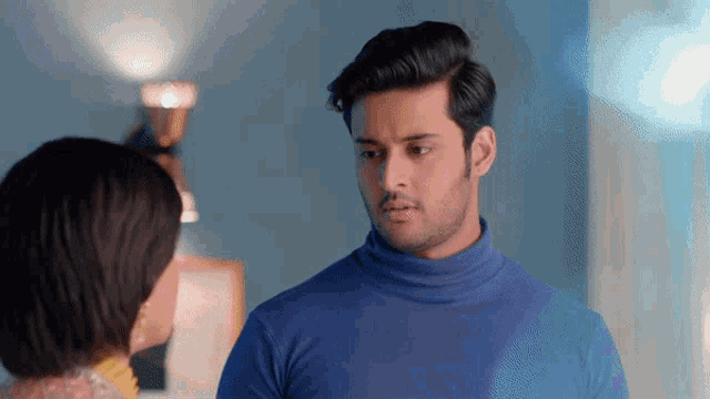 a man wearing a blue turtleneck looks at a woman