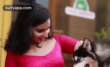 a woman in a pink dress is petting a husky dog on the head .