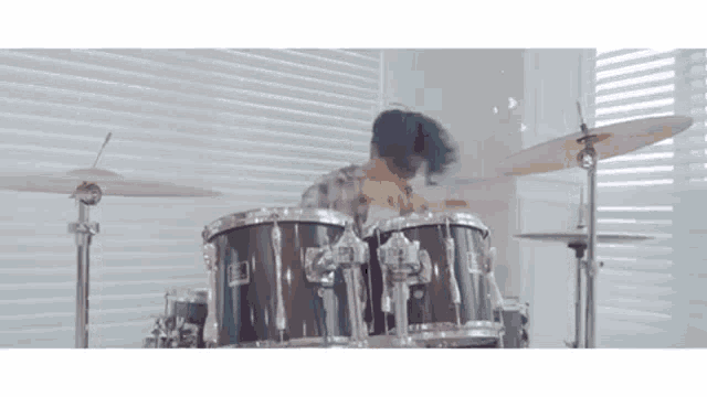 a man is playing a drum set in front of a window in a room .