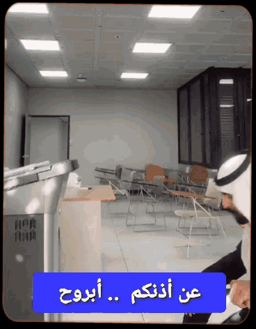 a man in a white turban sits in a classroom with a blue button that says " عن "