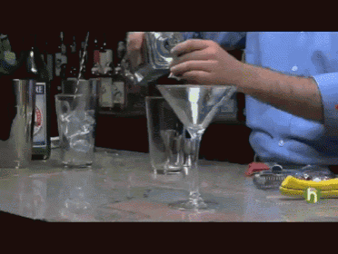 a bartender pours a martini into a glass