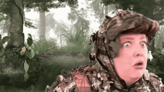 a man in a camouflage outfit is standing in the woods with his mouth open