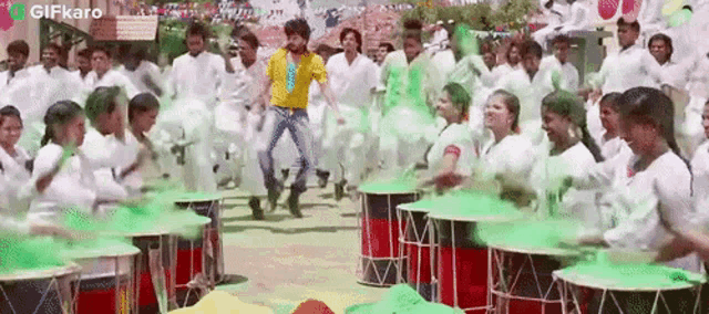 a man in a yellow shirt is jumping in front of a crowd of people playing drums