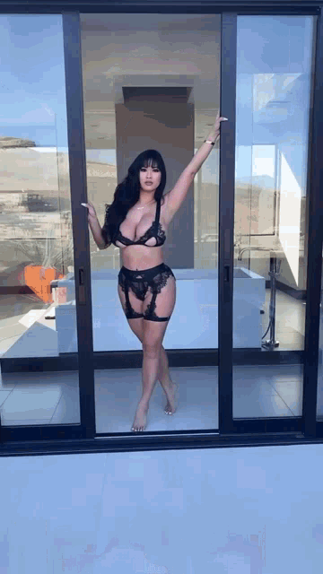 a woman in lingerie stands in front of a sliding glass door .