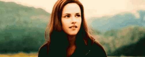 a woman with long brown hair is standing in front of a mountain range .