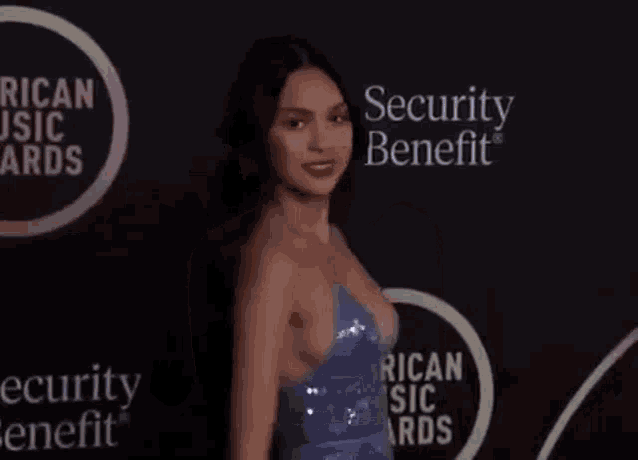 a woman in a blue dress is standing on a red carpet at an event .