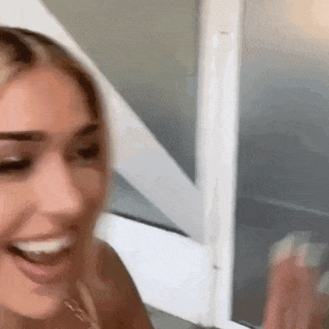 a woman is smiling and looking at herself in the mirror while standing in front of a window .