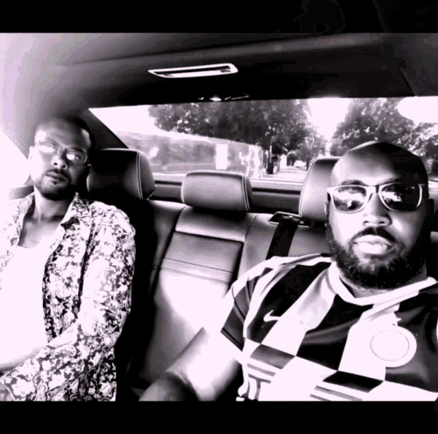 two men sitting in the back seat of a car one wearing a nike shirt