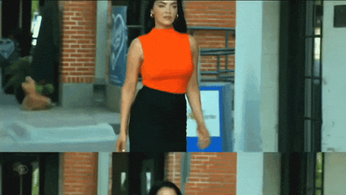 a woman in an orange top and black skirt is walking