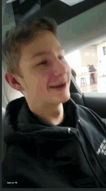 a young man in a black hoodie is smiling in the car