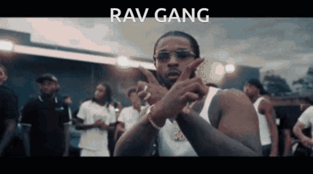 a man wearing sunglasses and a white tank top is standing in front of a crowd with the words rav gang written on the bottom
