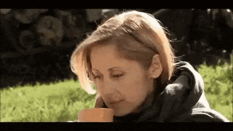 a woman is drinking a cup of coffee in the grass .
