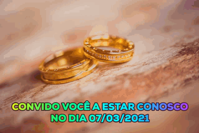 two gold wedding rings on a wooden surface with the words convido voce a estar conosco on the bottom