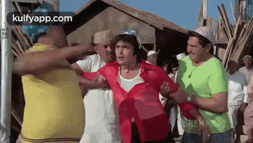 a group of men are standing around a man in a red shirt who is being held by another man .