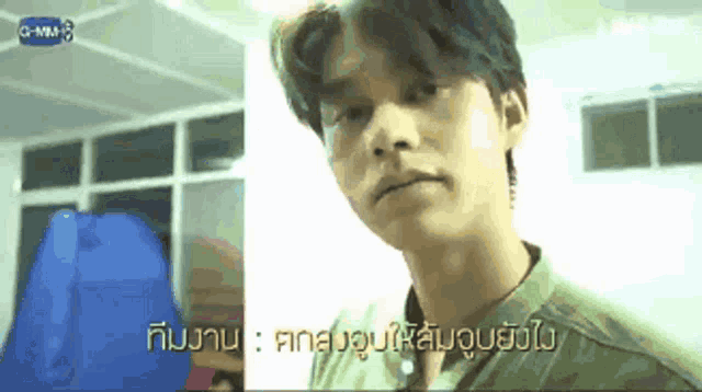 a man in a green shirt is making a funny face in a room with a blue bag in the background .