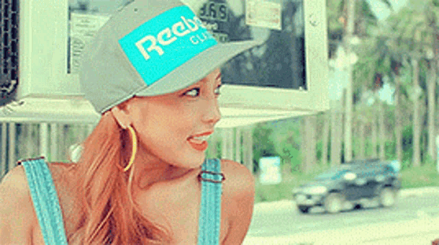 a woman wearing a reebok hat and overalls is smiling