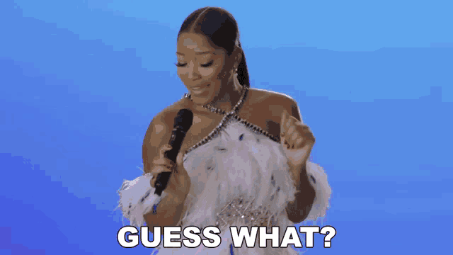 a woman in a feathered dress holds a microphone and says " guess what "