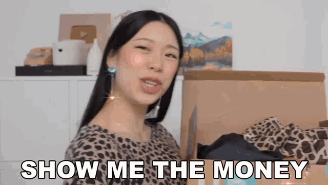 a woman in a leopard print shirt is standing in front of a cardboard box that says show me the money
