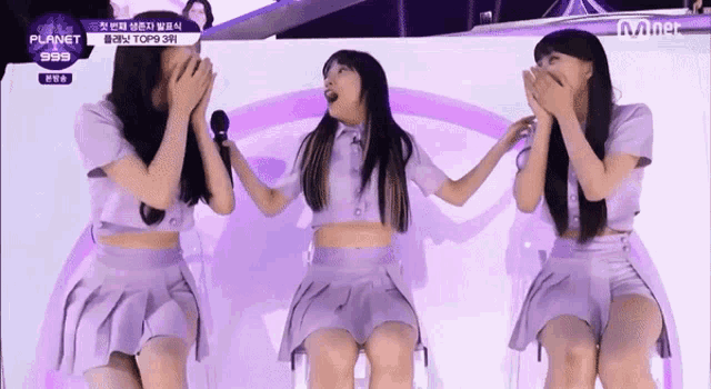 three girls in purple dresses are standing next to each other on a stage and one of them is holding a microphone .