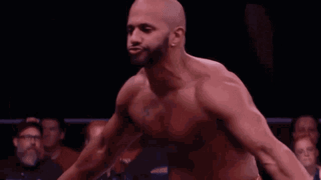 a shirtless wrestler with a tattoo on his chest flexes his arms