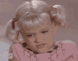 a little girl with pigtails is making a funny face while wearing a pink sweater .