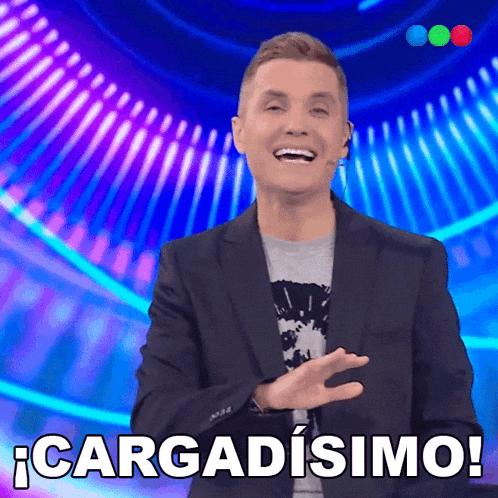 a man in a suit stands in front of a blue background that says cargadisimo