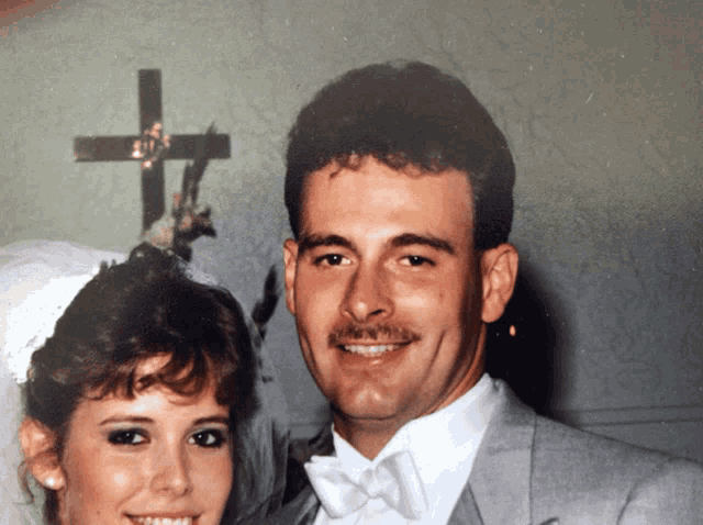 a man and a woman are posing for a picture in front of a cross