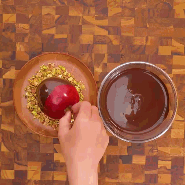 a person dipping a red apple in chocolate and nuts