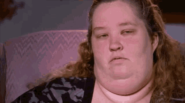 a woman with a very large neck is sitting in a chair and making a sad face .
