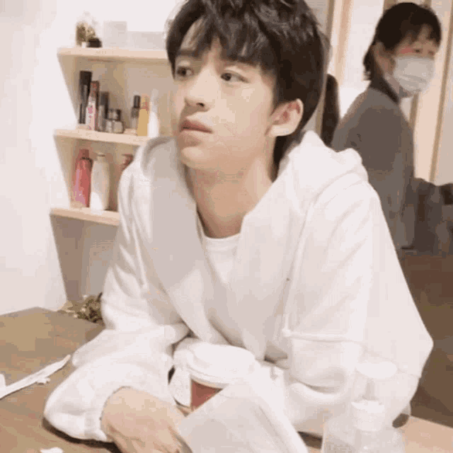 a young man in a white shirt sits at a table