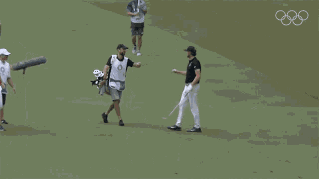 a group of men are walking on a golf course and one of them has a shirt that says tokyo 2020