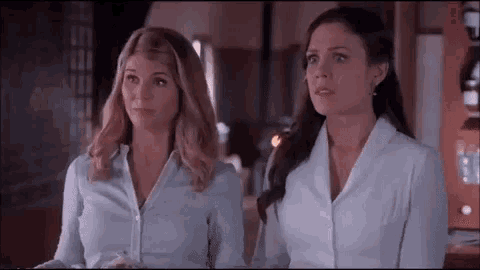 two women in white shirts are standing next to each other and looking at something .