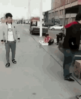 a man is walking down a sidewalk next to a woman sitting on the ground .