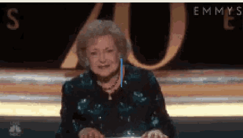 an older woman is sitting at a table in front of a sign that says emmys