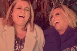 two women are sitting next to each other and laughing .