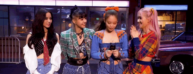 a group of girls are standing next to each other in front of a car and looking at a cell phone .