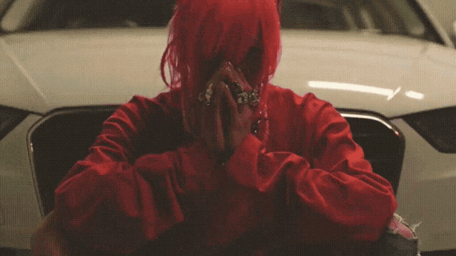 a woman with red hair is sitting in front of a white car with her hands folded