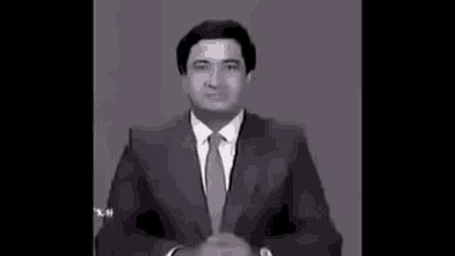 a man in a suit and tie is standing in front of a gray background .