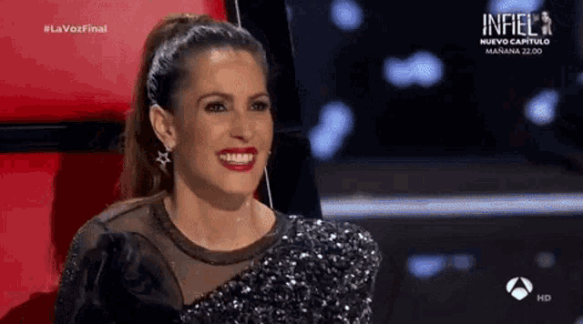 a woman in a sequined dress is smiling while sitting in a chair on a stage .