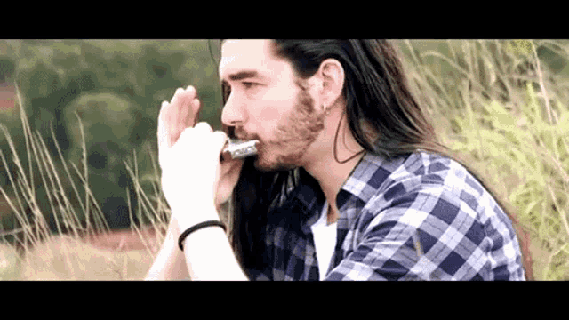 a man with long hair and a beard playing a harmonica